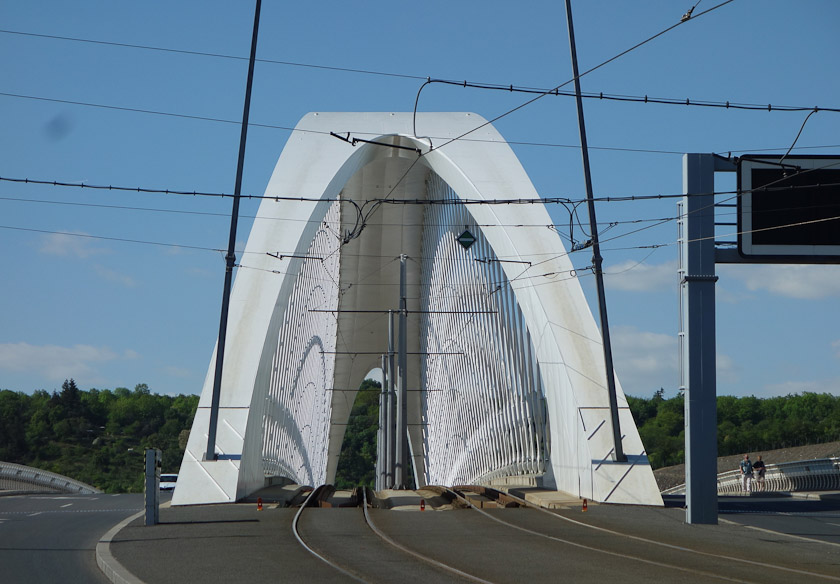The Troja Bridge crosses the Vltava north of Prague Castle. It is nine bridges downstream of the Charles Bridge. The roadway includes dual tram lines under the arch, car/bus/truck lanes on either side of the arch, and pedestrian/bike lines outside of those.