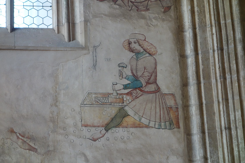 This minter is holding a die in his heft hand to impress the design on the face of the coin.
