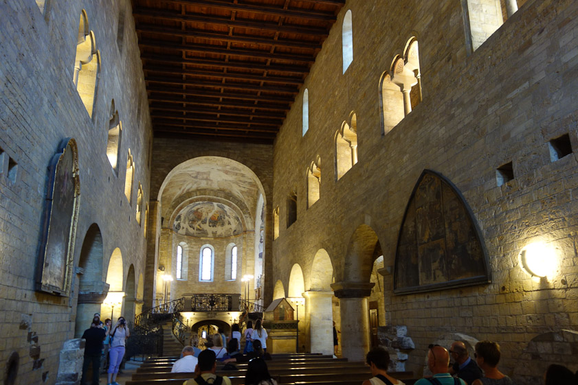 Heavy stone walls pierced by a few windows with round arches separate the nave from north and south aisles. Wood ceiling.