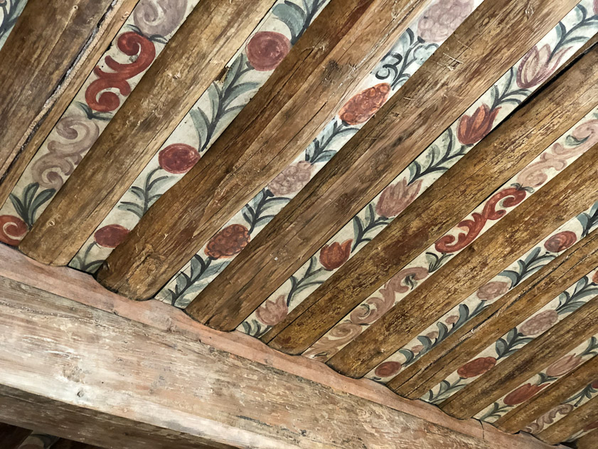 The spaces between the logs in the ceiling are spanned by painted strips of wood.