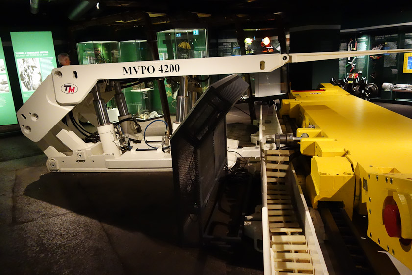 The yellow carriage, with revolving coal teeth at either end, moves in the direction into and out of the picture, ripping coal out of the ceiling. After making a pass, the white machine lowers slightly and moves to the right before going back up to hold the ceiling up. Tje whole apparatus thus enlarges a coal seam that is horizontal.