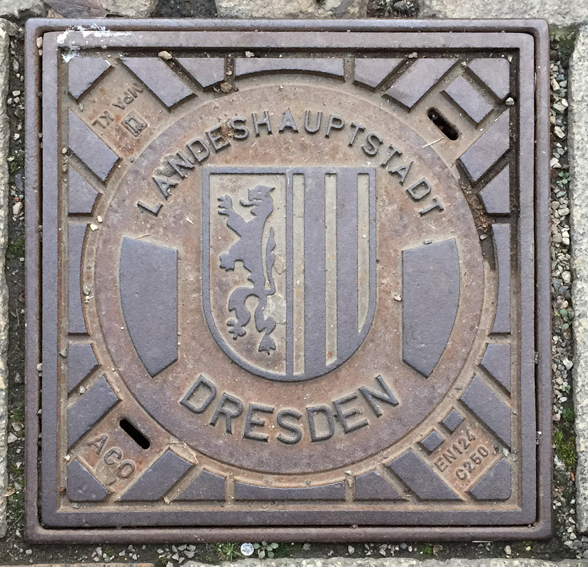A small street utility cover in Dresden, too small for a manhole but showing the city shield.