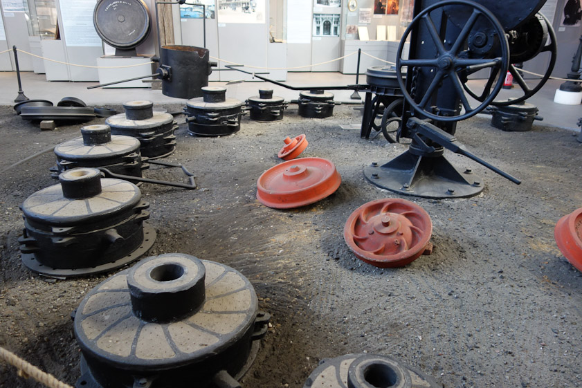 These are sand molds lying in a circle to be filled with molten metal from the bucket suspended from the rotating crane. The red objects are models used to make the sand molds. Two of these models are for railroad wheels.