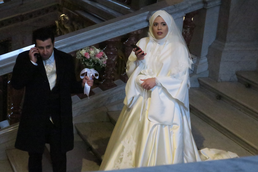 A Muslim bride and groom, busy with their phones on the staircase at the KHM during their parade past local sights.