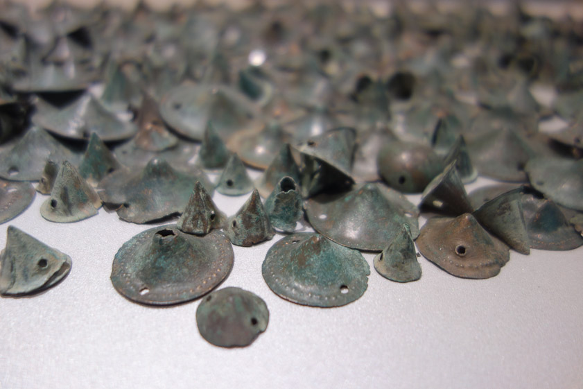 I believe these ornaments were attached by sewing or rivets through the holes, and are calle tutuli.