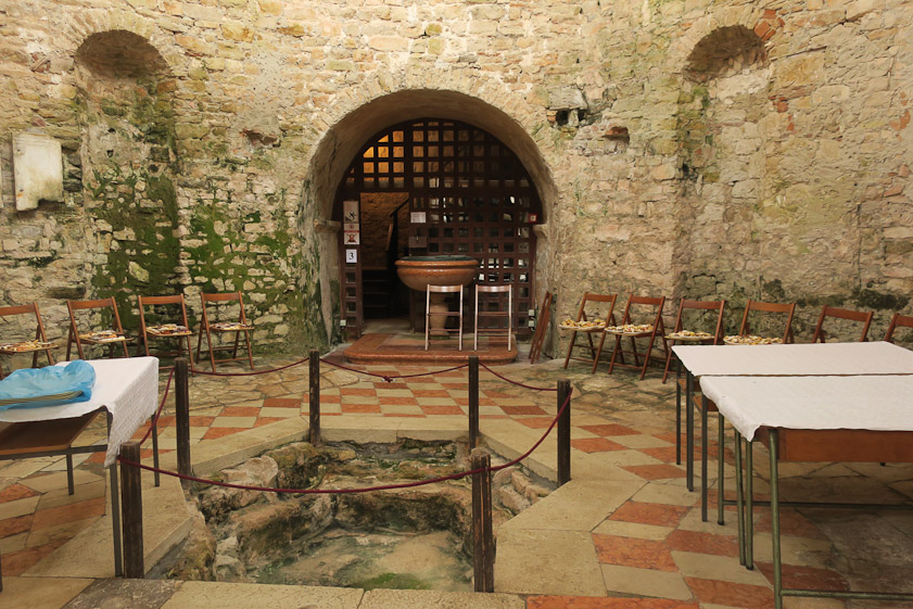 The baptistry has a mossy little basin for immersion. It was closed, being set up for some children's event. The bell tower is beyond the grate at the back.