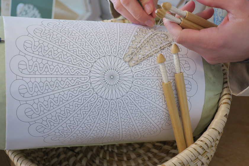 We later saw an example of bobbin lace being made. A pattern is wrapped around a pin cushion and pins are inserted and threads wrapped around them from many bobbins.
