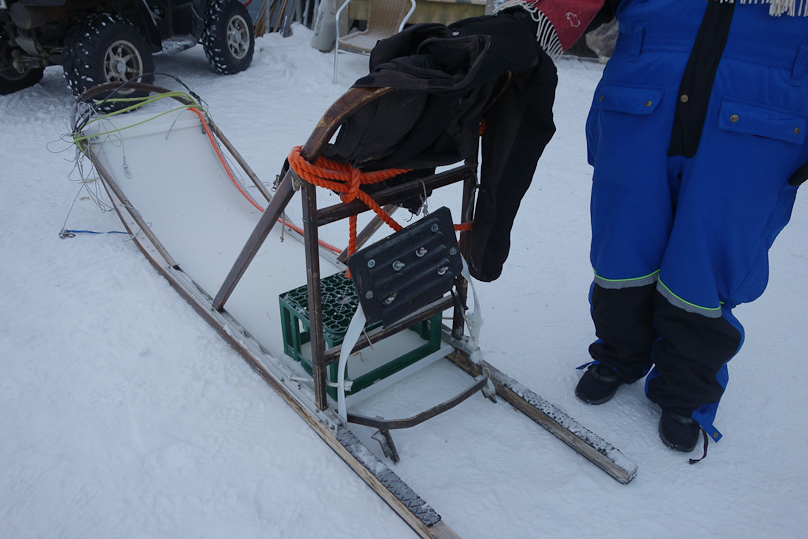 One passenger sat on a milk crate at the back of the sled, and the other sat between his legs, lower down. The driver stood on the runners in the back. The black plate was a brake, which the driver could step on to brake against the snow.