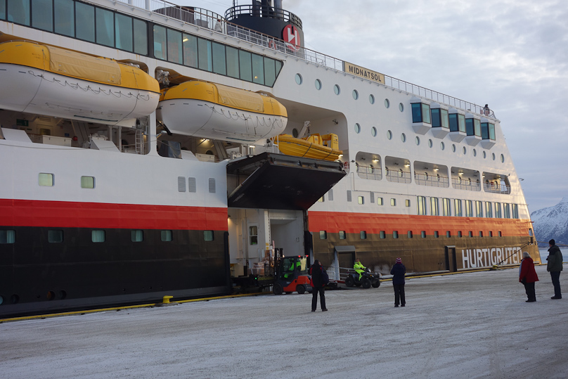 The ship at Sortland. A red forklift is unloading cargo as a four wheel all terrain vehicle drives off the ship.