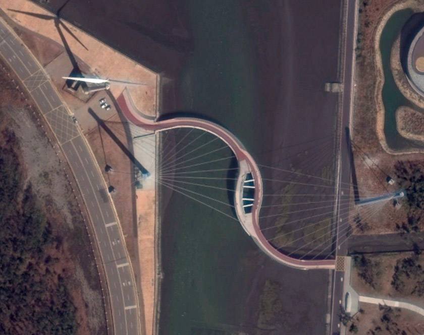I didn't understand that bridge until later, when I saw this Google Earth image. The blue mast is clear on the right, but the mast on the left is seen from above. Its shadow is clear, though. The white thing at the left end of the S-shaped bridge is a windmill.