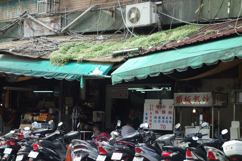 This in a busy commercial district of Taipei: a collapsing awning, a prolific weed, a tangle of electrical lines, and motor scooters.