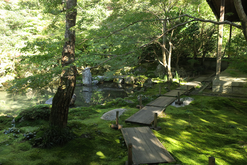 A wooden walk leads from the worship hall to the bell tower, with a pond on the left.