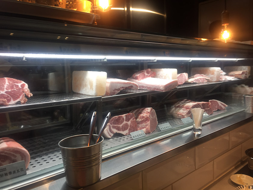 The meat cuts are displayed in a glass-front refrigerator with blocks of salt.