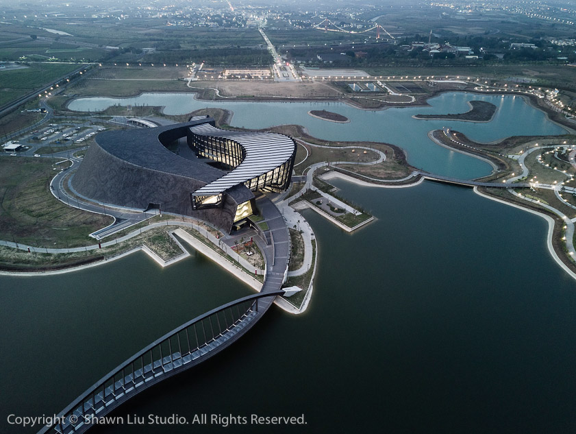 An architectural rendering of the museum. The white building is all glass, while the black building is faced with thousands of circular tiles.