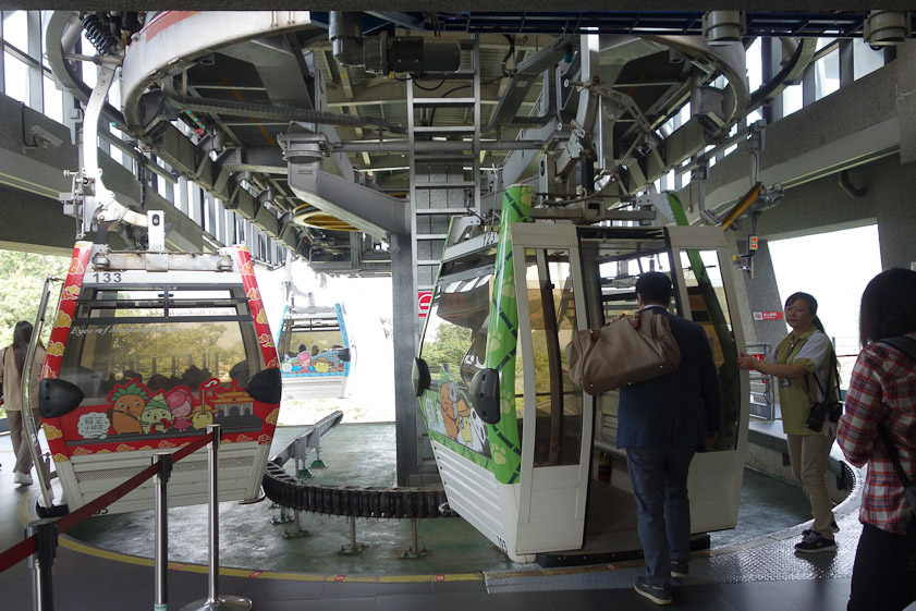 Cars detach from the fast moving cable between stations and connect to a slow moving cable in the station. They are never completely stopped.  Because of the speed differential cars are close together inside a staton.