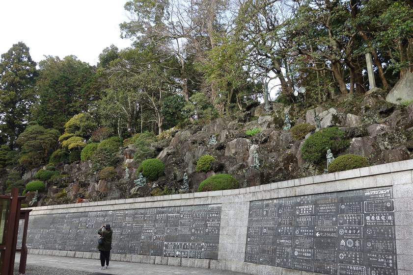 A wall with what may be grave markers holding back a steep, rocky hill where gardeners were trimming trees.