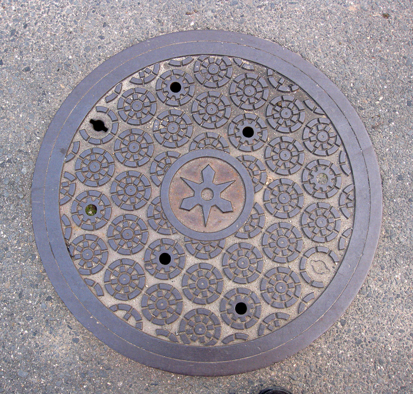 Manhole cover in the Arashiyama district of Kyoto. This shows fabric tied for shibori, before dyeing.