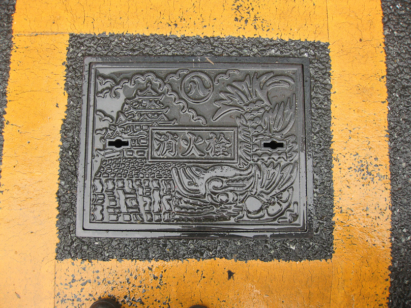 This is the manhole cover appendix that I promised you earlier in this slide show. If you get this far, you're hard core! This manhole cover is in Nagoya. Nagoya Castle is shown on the left. The figure on the right is the carp (tail at the top, head on the bottom) that appears at the ends of the ridge on Nagoya Castle. The middle kanji in the center means fire, so this probably covers a fire hydrant.