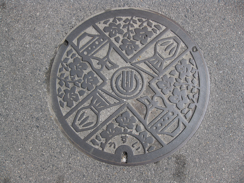 Manhole cover in Toki City. Toki is the center of the Mino ceramic area, which is reflected in the various pots in this design. The kana read usui which means rain water, so this probably covers the storm sewer.