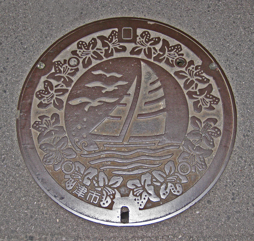 Manhole cover in Tsu, capital of Mie Prefecture. The kanji read tsushi (Tsu City). Tsu is on Ise Bay, hence the sailboat and waves and gulls.