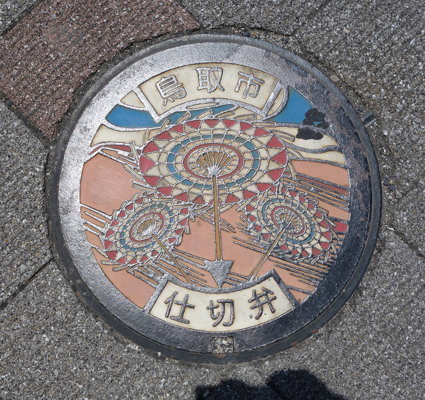 Manhole cover in Tottori. We stopped here for lunch en route from Matsue to Kinosakionsen. The umbrellas presumably refer to the local festival, which features dances with umbrellas.