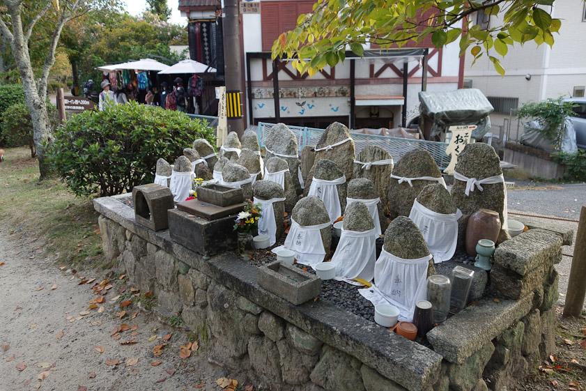 Little group of stones along the Philosophers' Walk. I'd guess Shinto, and Mariana thinks they stand for dead children, each has a white bib vicee the red bibs seen at Nikko Botanic Garden. Upturned-bottles and vases for flowers? Little soufflé cups for food?