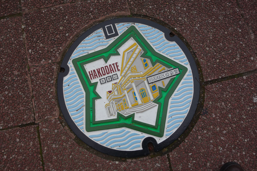 Painted manhole cover in Hakodate. The five-pointed Goryokaku fort is far from the Former Public Hall of Hakodate Ward （旧函館区公民館）. The cover gives access to the sewer (おすい).
