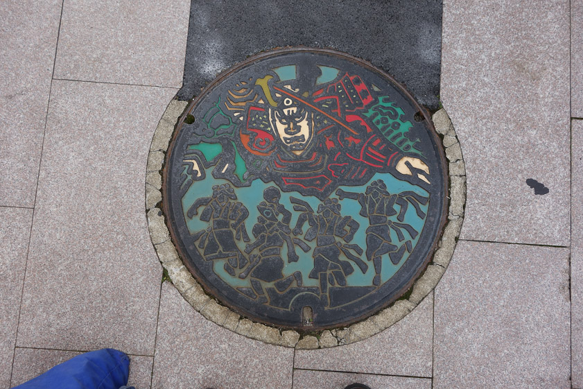 Manhole cover in Aomori, home to the Nebuta Matsuri, a festival featuring floats like that at the top.