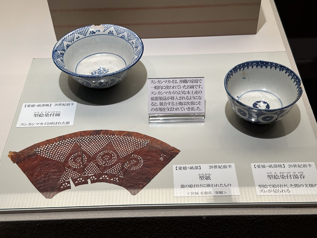 The object at lower left is a stencil for transferring a pattern of glaze to something larger than the two bowls shown with it.Traditional stencil paper, shibugami, is made of several layers of handmade mulberry paper which are strengthened with persimmon tannin and then smoked.
