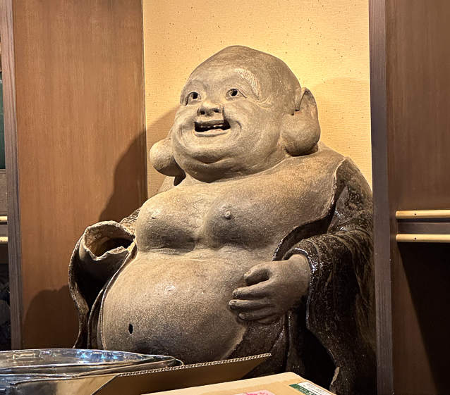 An old damaged happpy, fat Buddha, symbol of prosperity found in many teahouses.