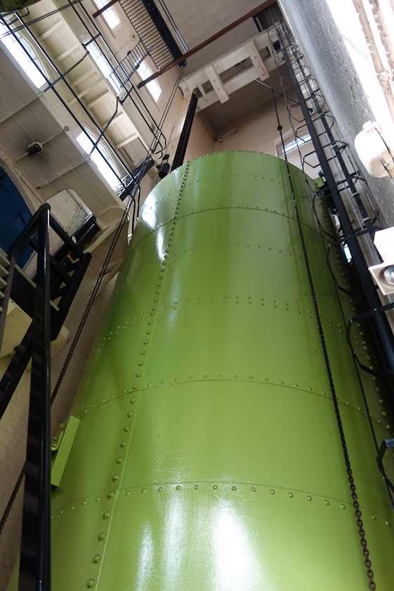 An accumulator is a 100-ton green cylinder raised by a piston to store potential energy.
