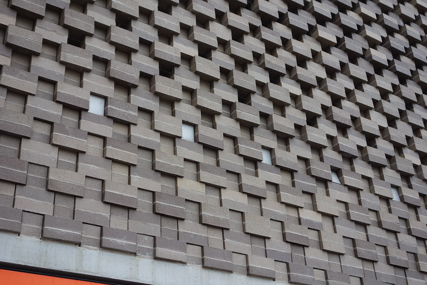 The stepped brickwork is made possible by steel rods threading through the bricks. This allows the surface to conform to the tilted planes of the structure. Also the small perforations, let light out at night.