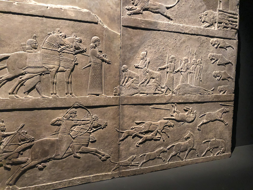 In the top register lions are released from cages into the hunt grounds. TBelow this, the dead lions are shown to the king. Below, he fires arrows into a fleeting herd of gazelles. See https://en.wikipedia.org/wiki/Lion_Hunt_of_Ashurbanipal