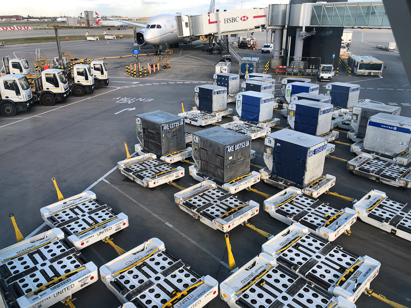 En route to our plane we passed these lower bay cargo containers, all of type AKE. The yellow bars appear to be brakes that hold the containers in place until time to move into the aircraft. There is a belt in the middle of the white trailers that moves the container onto the aircraft. See https://en.wikipedia.org/wiki/Unit_load_device