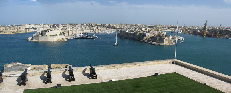 View of the Grand Harbor from the Saluting Battery at the southeast corner of Valletta. The promintory at the left is Birgu, with Fort St. Angelo at its tip and with the black Maltese Falcon moored to its right. The promontory to the right of center is Senglea, with Fort St. Michael. These two promontories were held by the Knights of St. John during the Great Siege of 1565.