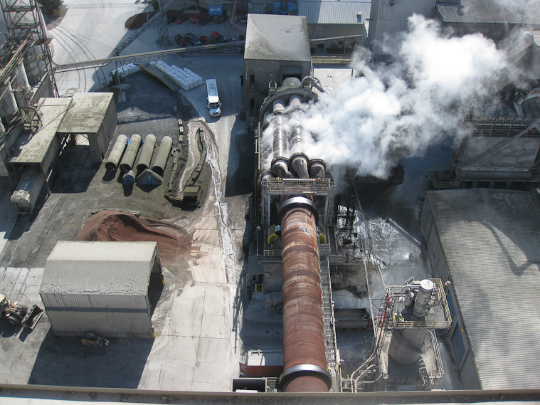 View from the 240 foot high preheater tower. The rusty tube in the foreground is the kiln; it is rotating, as are the nine coolers, which are steaming with cooling water.