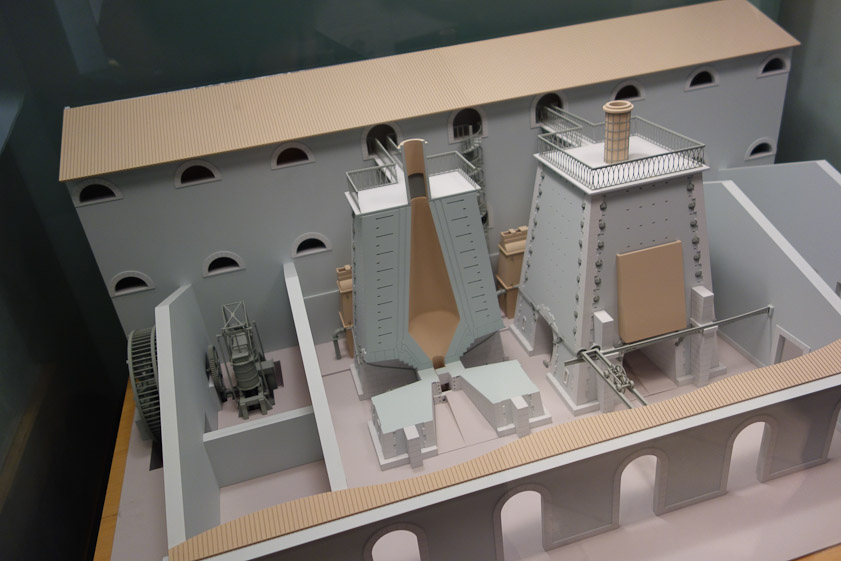 Model of two blast furnaces. The water wheel at the left drove an air pump that supplied air to the furnaces, where coal or coke, limestone and iron ore were burrned. Those ingredients entered the furnaces at the top and molten iron flowed out the bottom. The furnaces were named 