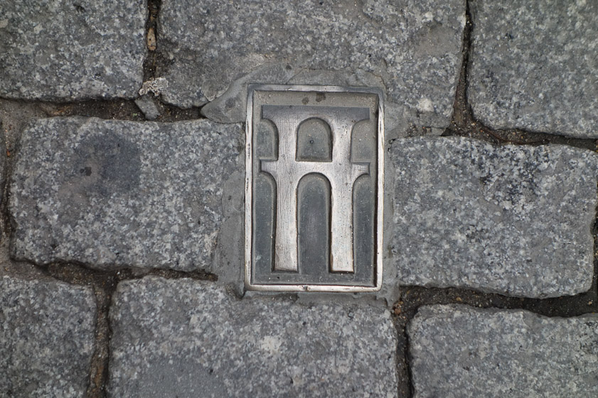 Bronze marker in the street above the course of the underground aqueduct. The water flowed in an open channel within a tunnel that dates from the 15c. The Roman distribution system is unknown.