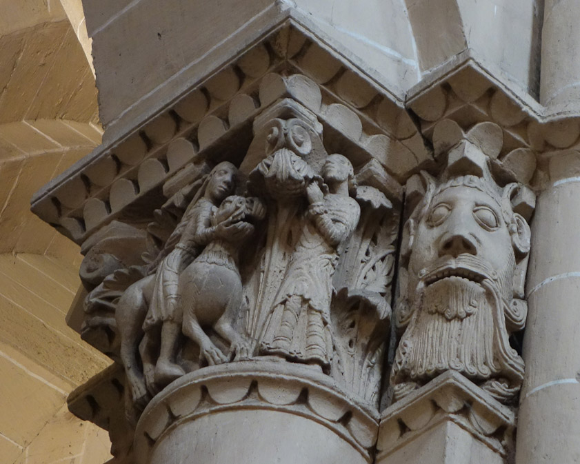 The sharpest photo of this capital that I took. The woman's left hand is seen pulling up the cat's jaw. This is a variant on frequent representations of Hercules killing the Nemean lion (the first of his labors), and Samson killing a lion as recounted in Judges 14:5. The huge man's face may be a Green Man, with tendrils growing out of the corners of his mouth.