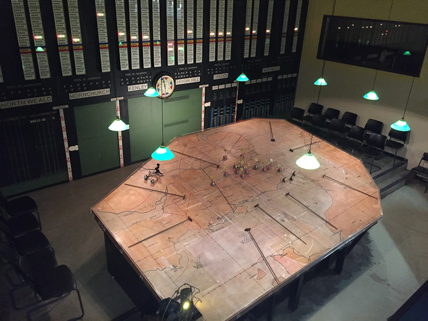 The Group commander commited his fighter forces from this viewpoint. Each white column on the back wall indicated the status of a single RAF squadron (Hurricanes and Spitfires) at the airbases named below (North Weald et al.). Radar and visual observers sent data to a filter center that forwarded it to headsets worn by the women.