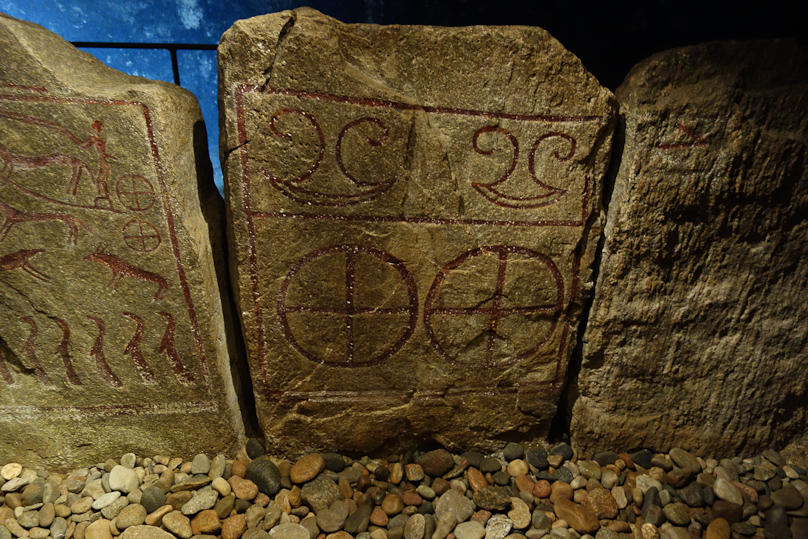 The quartered circles are called sun-wheels, and are common Bronze Age symbols. The rocker symbols depict axe heads.