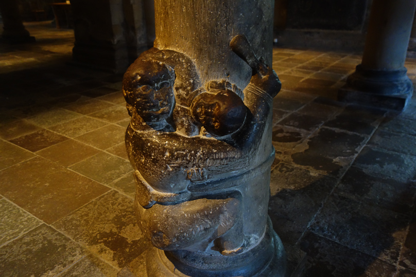 What looks like a short cudgel in his right hand is actually the end of the rope he is holding the column together with. He appears to be squeezing someone against the column.
