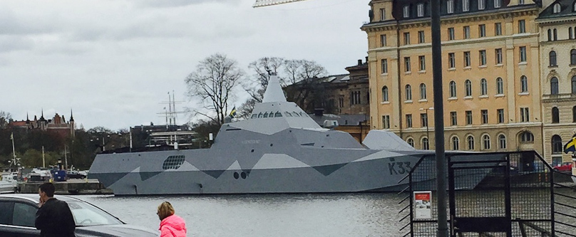 On our second full day in Stockholm we were on a bus to Djurgården when we saw this camouflaged low observable warship, the HSwMS Härnösand, a Visby-class corvette. The light gray structure above the K on its bow is the gun turret, with the gun barrel hidden to reduce its radar cross  section. I presume the grill behind the superstructure is the air inlet or exhause for its engines.